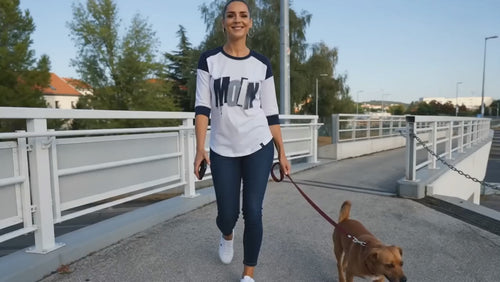 Frau trägt Damen Raglan-Shirt mit 3/4-Ärmeln in True Navy/White – New Era LNEA104 mit Moin-Print, sportlicher Baseball-Look beim Spaziergang mit Hund