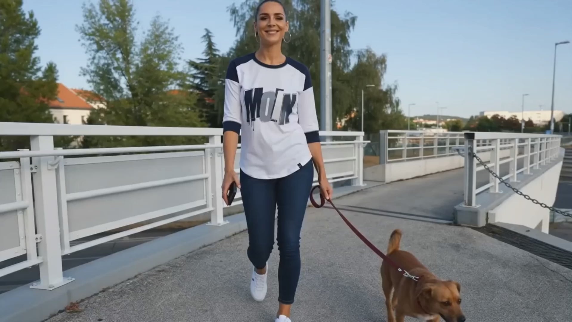Frau trägt Damen Raglan-Shirt mit 3/4-Ärmeln in True Navy/White – New Era LNEA104 mit Moin-Print, sportlicher Baseball-Look beim Spaziergang mit Hund